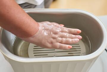 Eine Hand wird in flüssiges Paraffin getaucht.
