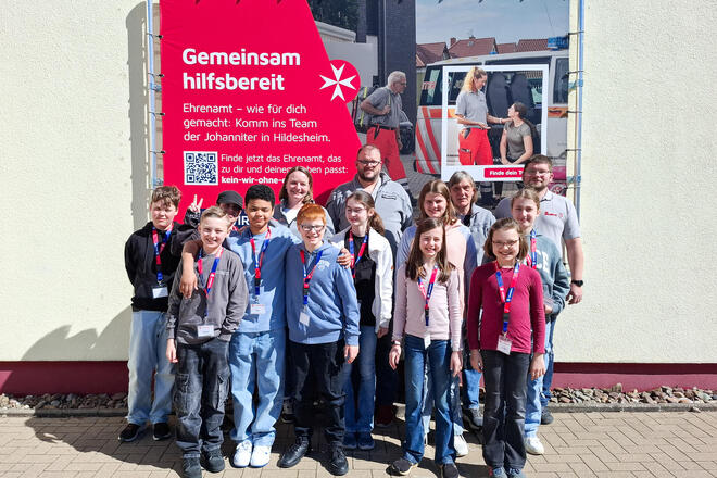 Kinder und ein Mann stehen draußen vor einer Wand.