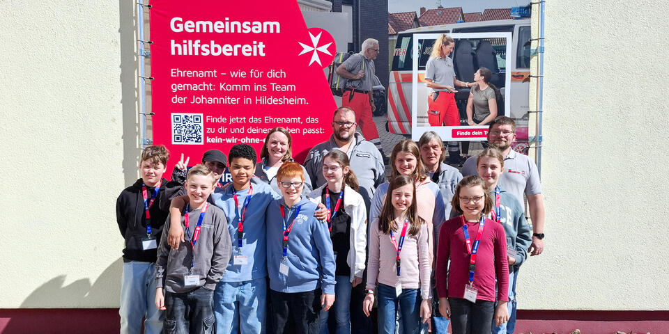 Kinder und ein Mann stehen draußen vor einer Wand.