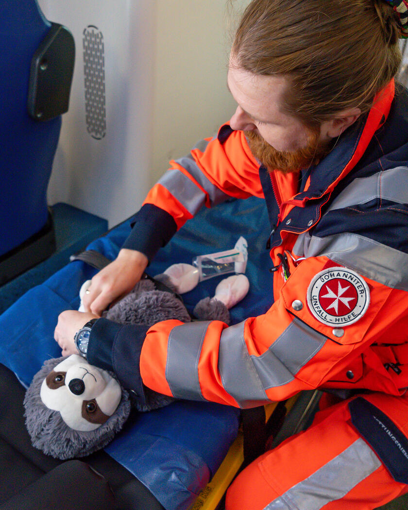 Tag der offenen Tür Lübeck 2025 Ein Rettungssanitäter der Johanniter verbindet einem Kuscheltier dem Arm. Das Kuscheltier liegt auf einer Trage in einem Rettungswagen.