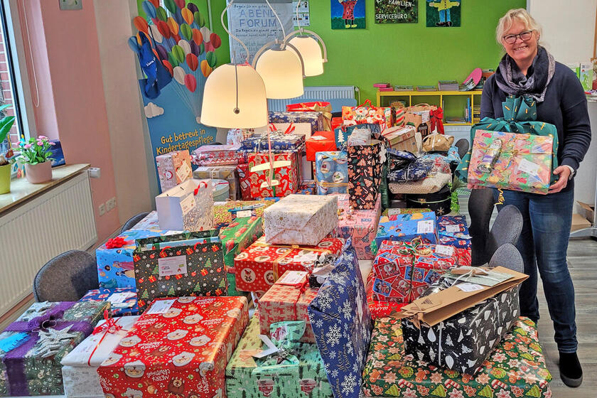 Eine Frau steht an einem Tisch, auf denen zahlreiche weihnachtlich verpackte Geschenke liegen.
