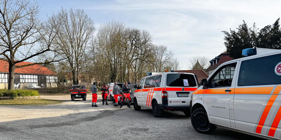 Einsatzkräfte mit Mannschaftstransportfahrzeugen auf einem Platz. Im Hintergrund Bäume und ein Fachwerkgebäude. 
