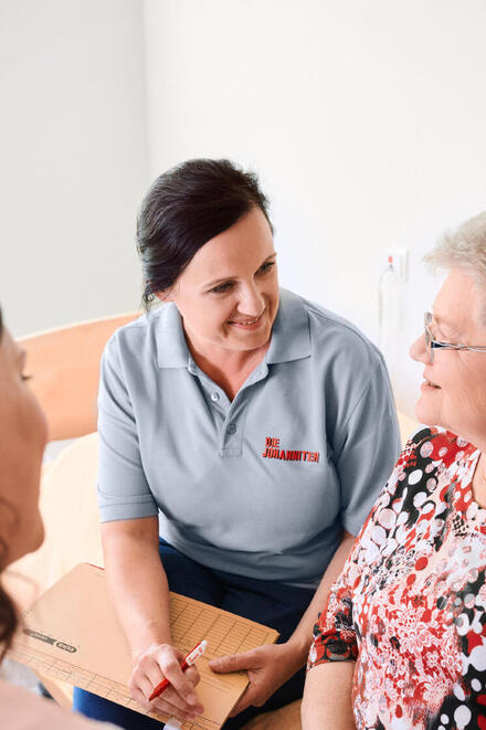 Eine Mitarbeiterin der Johanniter im Gespräch mit einer älteren Frau.