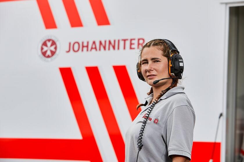 Eine Ehrenamtliche der Johanniter steht mit Headset vor einem Rettungswagen auf dem Deichbrand Festival 2022.