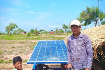 Ein Mann und sein Sohn neben einer solarbetriebenen Wasserpumpe auf einem Feld.