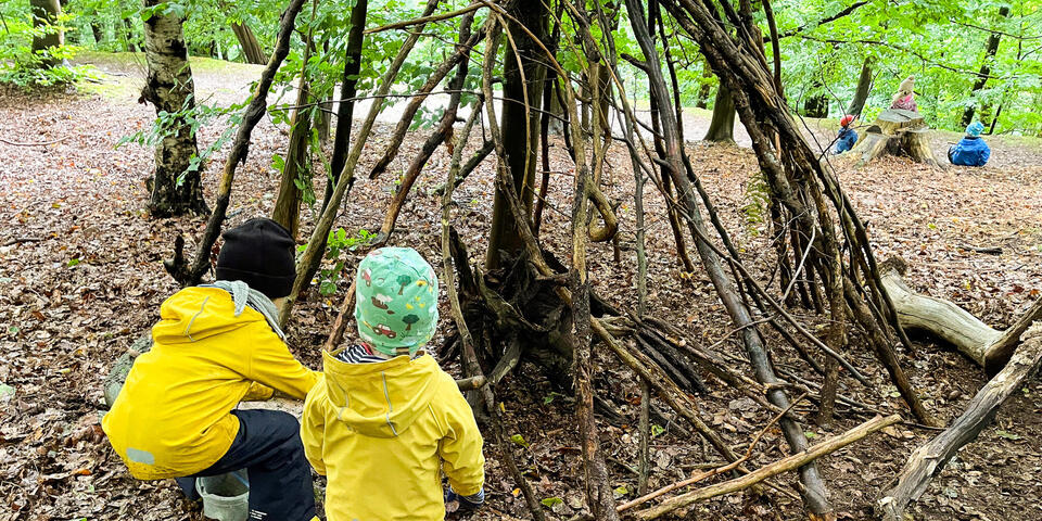 Zwei Kinder in einem Wald. Sie errichten ein Holztipi