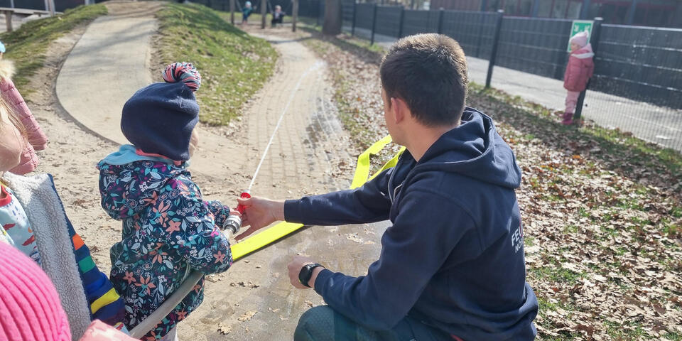 Ein Feuerwehrmann hilft einem Kind, das einen Schlauch hält