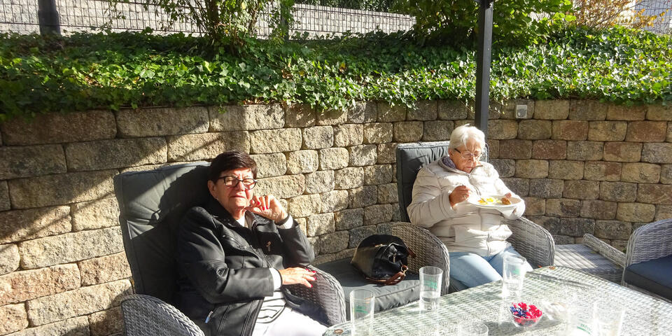 Zwei ältere Damen sitzen in Gartenstühlen.