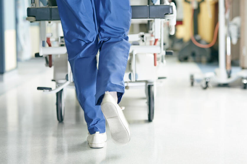 Krankenhauspersonal schiebt ein Krankenbett, Ansicht der Beine und der Rollen des Betts.