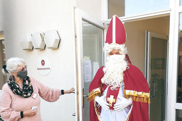 Eine grauhaarige Frau mit einem Mundnasenschutz öffnet einem als Nikolaus verkleideten Mann die Tür.