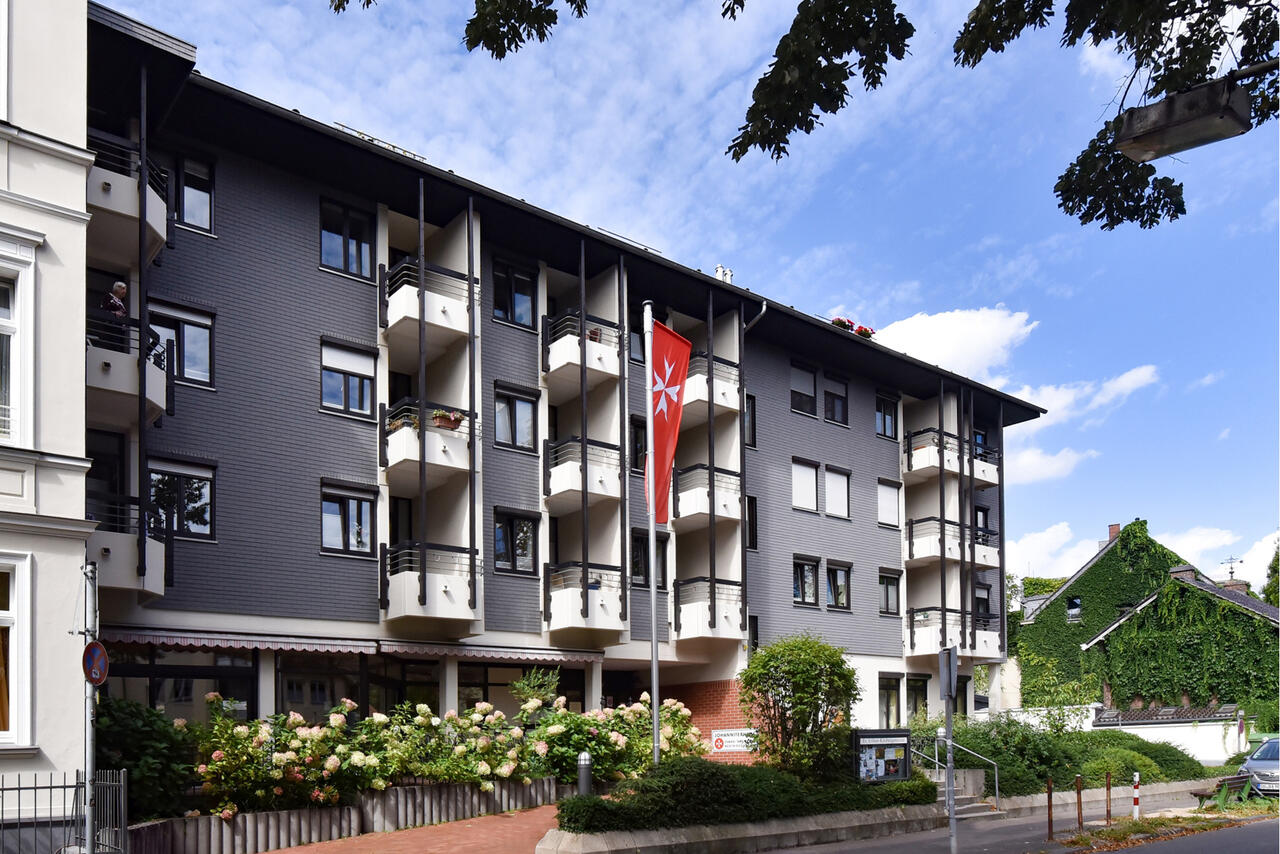 Mehrstöckiges dunkel verklinkertes Haus mit vordere Blumenrabatte.