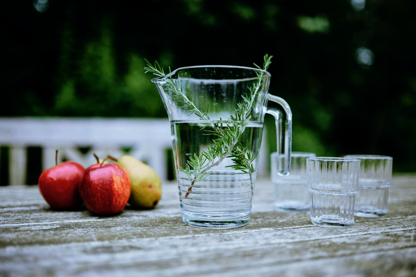 auf einem Gartentisch liegen Äpfel, daneben stehen ein Krug mit Wasser und mehrere Gläser
