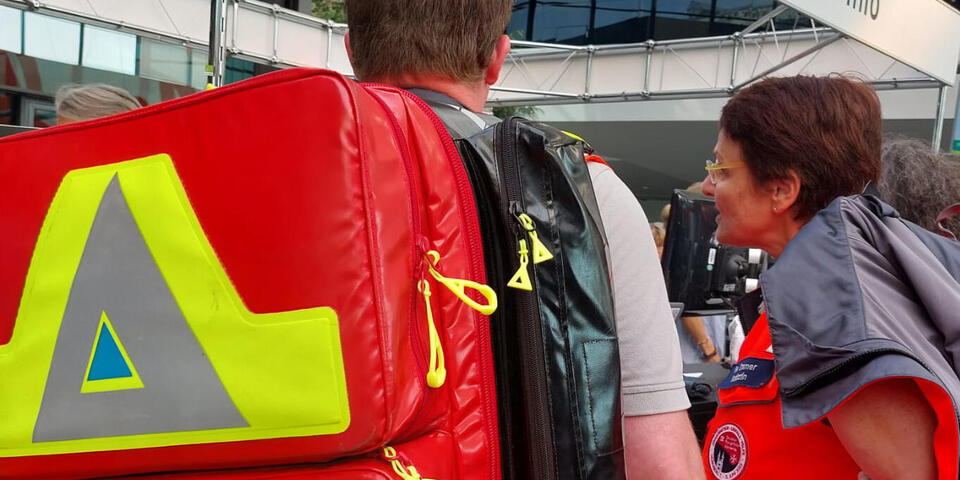 Eine Johanniterin und ein Johanniter mit Notfallrucksack an einem Informationspunkt