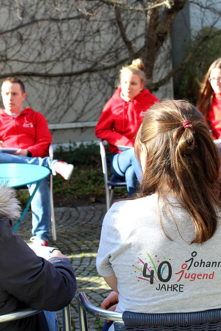 Eine Gruppe von jungen Menschen sitzt in einem Stuhlkreis und unterhält sich. Alle tragen Johanniter-Jugend-Kleidung.