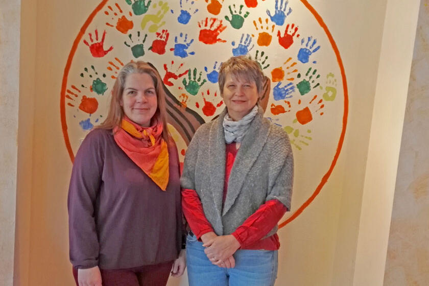 Tanja Gutknecht und Britta Thater-Mattke steht vor einen Zimmerwand mit bunten Handabdrücken. 
