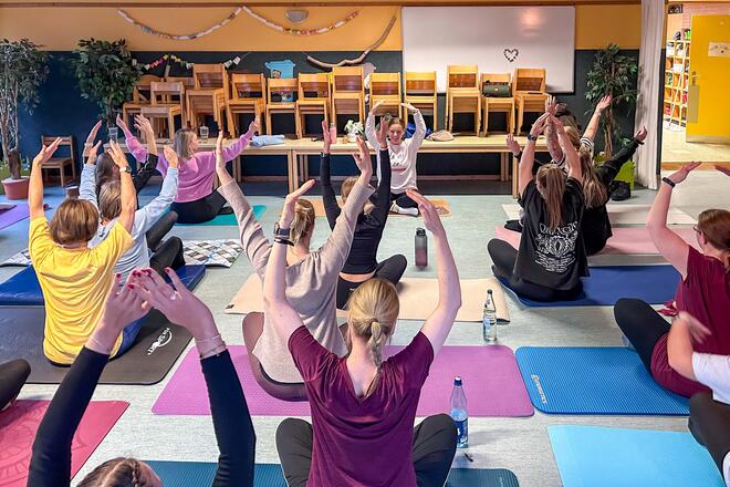 Teamtag in der Kita Hemdingen Eine Gruppe von Menschen macht Pilates: Alle sitzen und heben die Arme in die Luft.