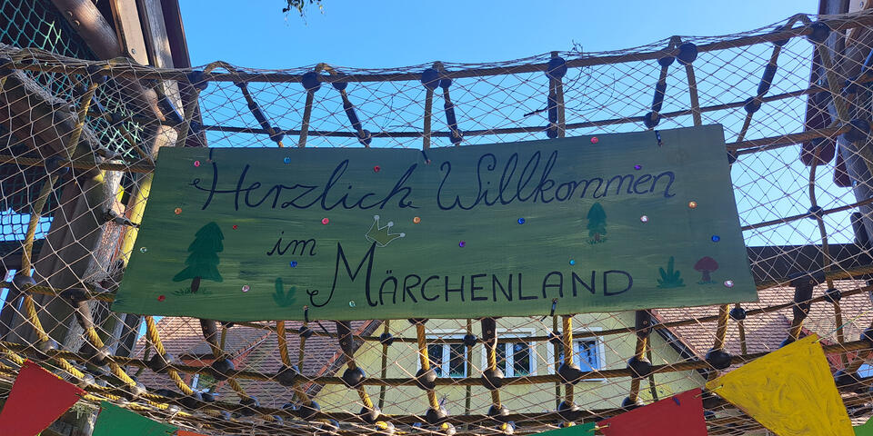 Ein Banner mit Herzlich Willkommen im Märchenland umgeben von Wimpeln vor einem Haus