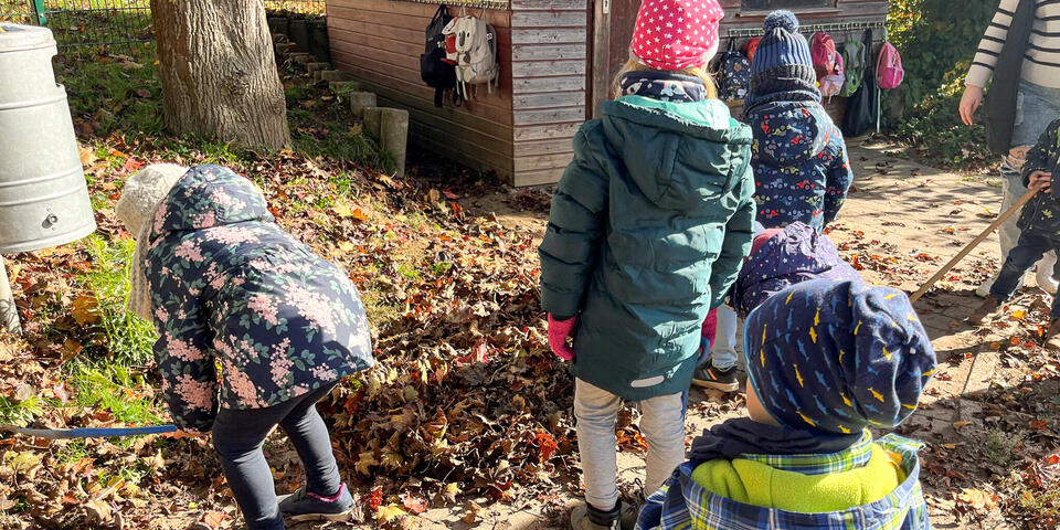 Kinder schieben einen Laubhaufen zusammen