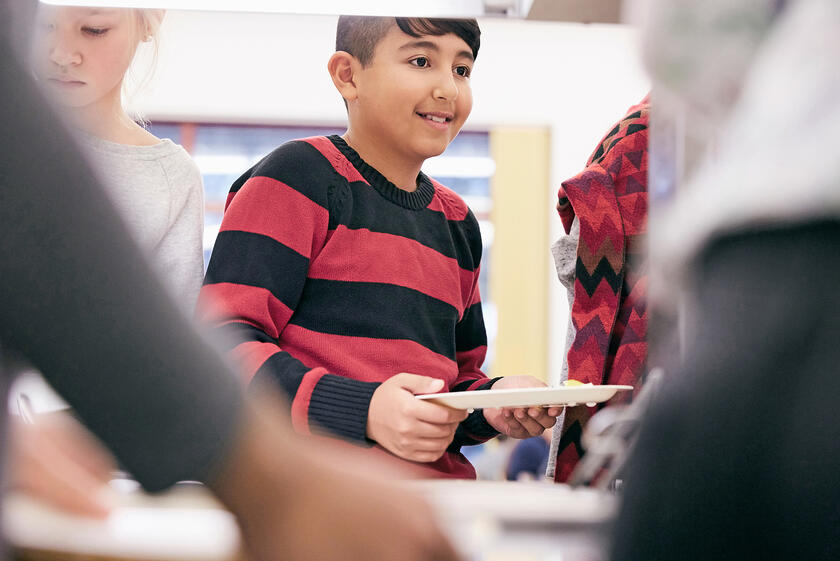 Kind steht erwartungsvoll mit Teller vor Essensausgabe