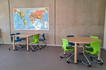 Tische mit grünen und blauen Stühlen vor großer Weltkarte im Hort-Lernraum.