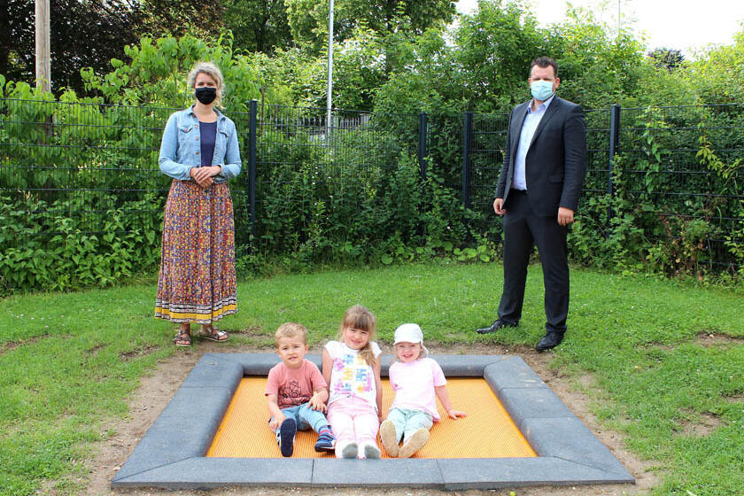 Drei Kinder sitzen auf dem neuen Trampolin, an der Seite steht die Kita-Leitung und der Klinikgeschäftsführer des Hildesheimer Helios Klinikums.