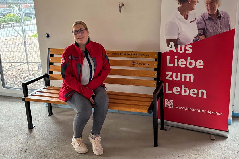 Inken Bär sitzt auf einer Gartenbank neben einem Rollup der Johanniter.