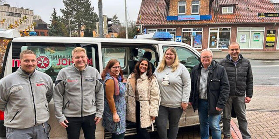 Zwei Johanniter, zwei Frauen und zwei Männer vor einem mit Weihnachtstruckerpaketen vollbeladenen Johanniter-Transporter