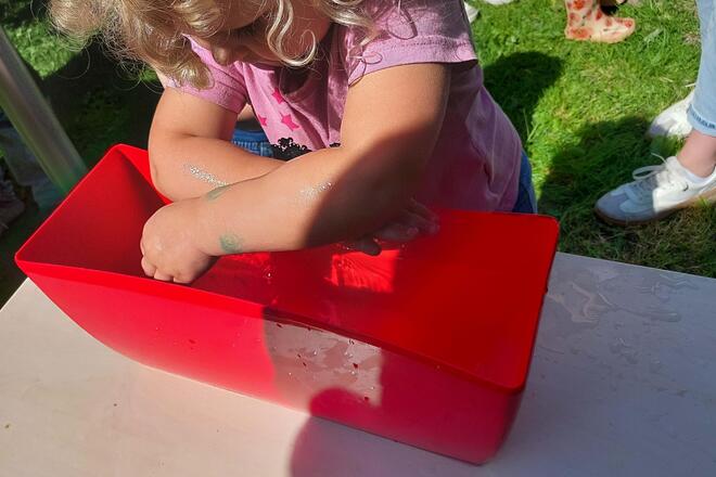 Kneipp-Sommerfest der Johanniter-Kita Sternschnuppe Ein Kind taucht seine Unterarme in eine Wanne mit Wasser.