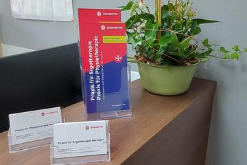 Auf einer Theke stehen Flyer und Visitenkarten der neuen Praxis sowie eine Grünpflanze