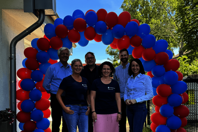 drei Männer und drei Frauen stehen in einem Bogen aus roten und blauen Luftballons.