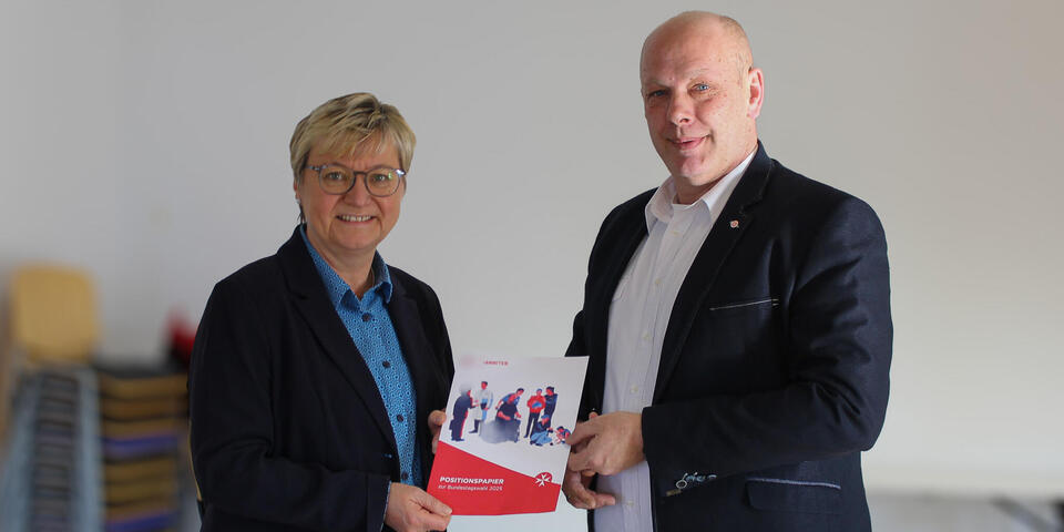 Ein Mann überreicht einer Frau eine Broschüre. Auf der Broschüre ist "Positionspapier" zu lesen.