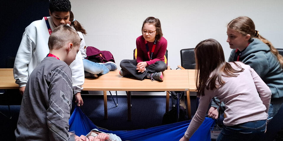 Kinder tragen eine Person in einer Rettungdecke