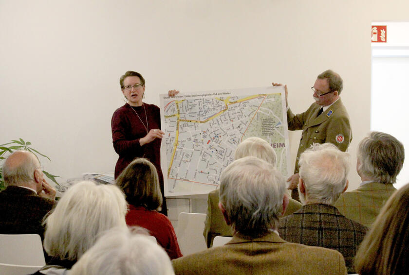 Ein Mann und eine Frau halten ein Bild mit einem Stadtplan vor Zuschauern hoch