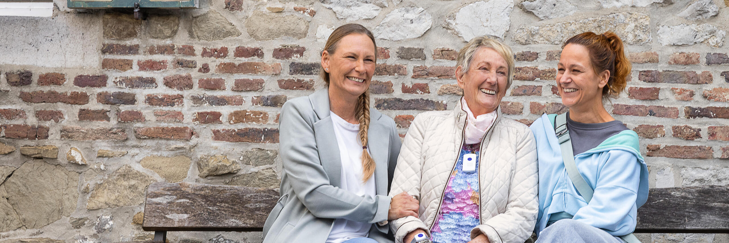 Eine Hausnotruf Teilnehmerin zusammen mit ihren Töchtern sitzend auf einer Bank.