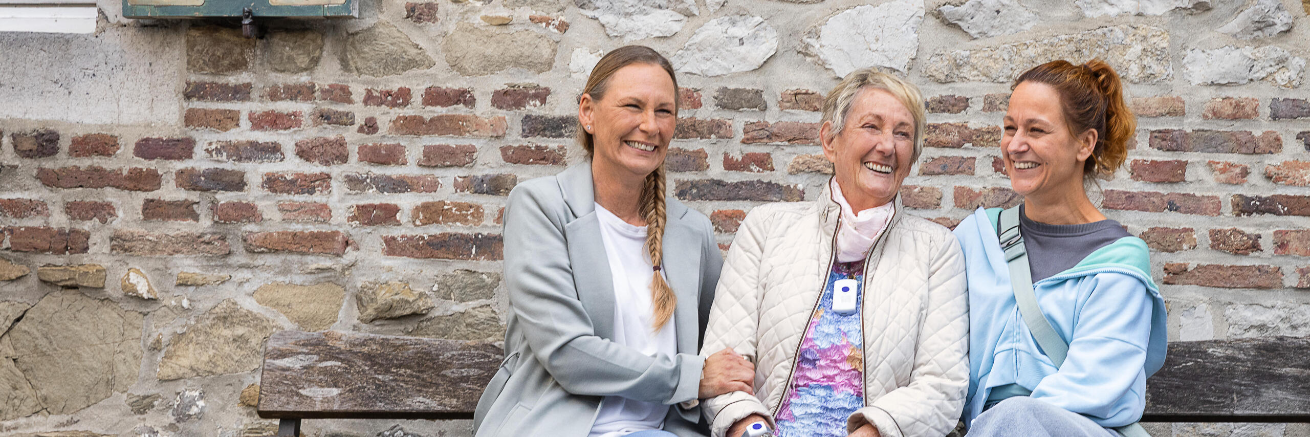 Eine Hausnotruf Teilnehmerin zusammen mit ihren Töchtern sitzend auf einer Bank.