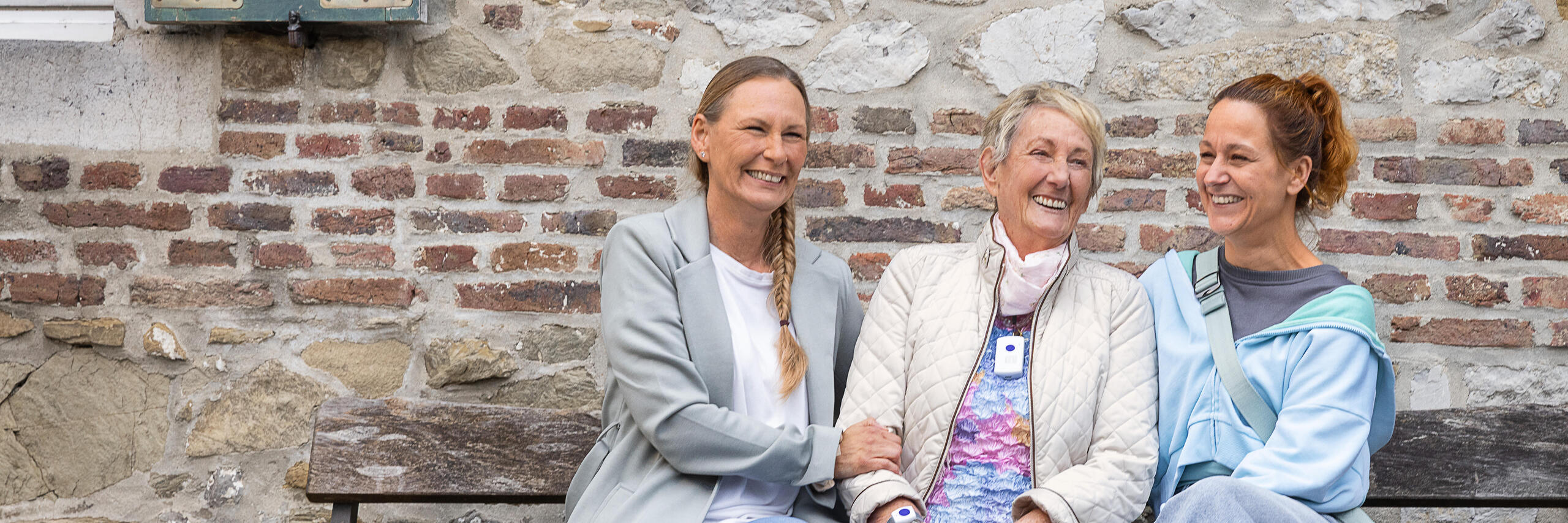 Eine Hausnotruf Teilnehmerin zusammen mit ihren Töchtern sitzend auf einer Bank.