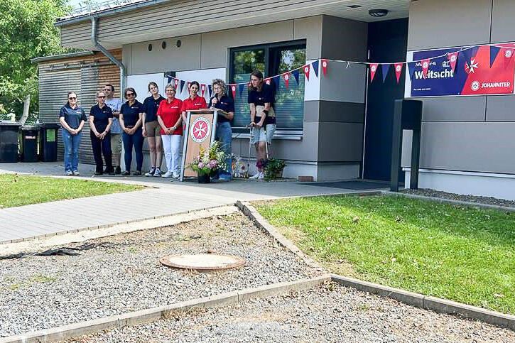 Neun Johanniterin vor einer Kita. Eine spricht an einem Rednerpult in ein Mikrophon