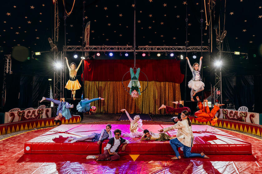Kinder in bunten Kostümen zeigen Akrobatik im Zirkuszelt.