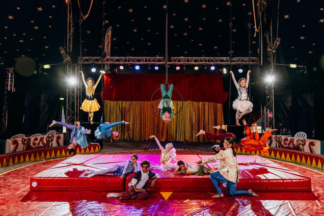 Kinder in bunten Kostümen zeigen Akrobatik im Zirkuszelt.