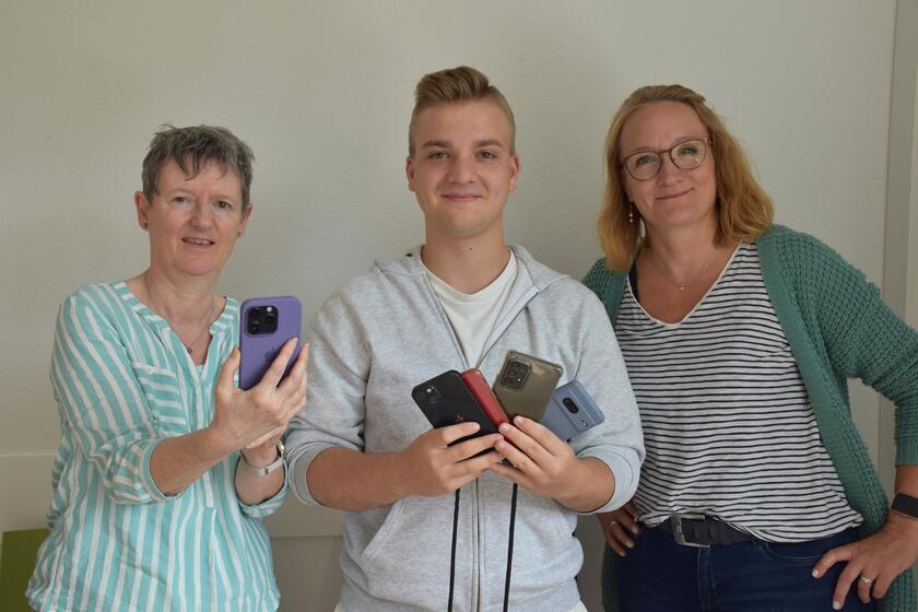 Kirsten Wienand, Moritz Jodjohn und Sandra Petersen von den Johannitern zeigen ein Handy hoch und werden die Handysprechstunde durchführen