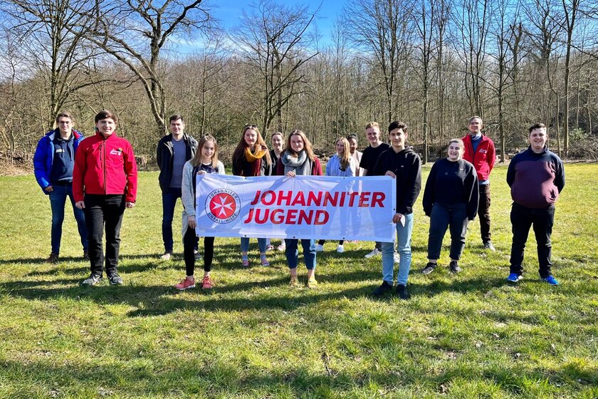 Gruppenbild der 13 Teilnehmer:innen auf einer Wiese. Vorne das Johanniter-Jugend-Banner.