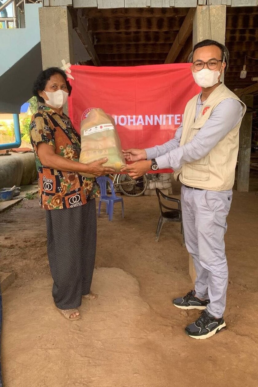 A KCD staff member hands a bag with hygiene utensils to a woman. Both wear face masks