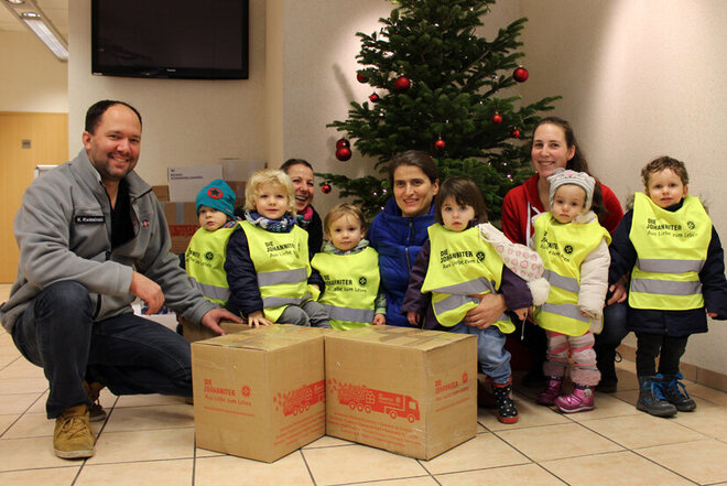 Johanniter und eine kleine Gruppe der Ostendkinder gemeinsam mit den gepackten Pakete vor dem Weihnachtsbaum in der Regionalgeschäftsstelle der  Johanniter in Hildesheim. 