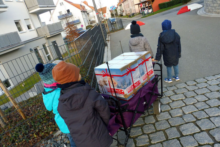 Kita-Kinder ziehen gemeinsam einen Bollerwagen auf dem sich ein Paket für die Weihnachtstrucker befindet.