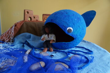 Ein blauer Fisch aus Pappe mit einer Puppe davor