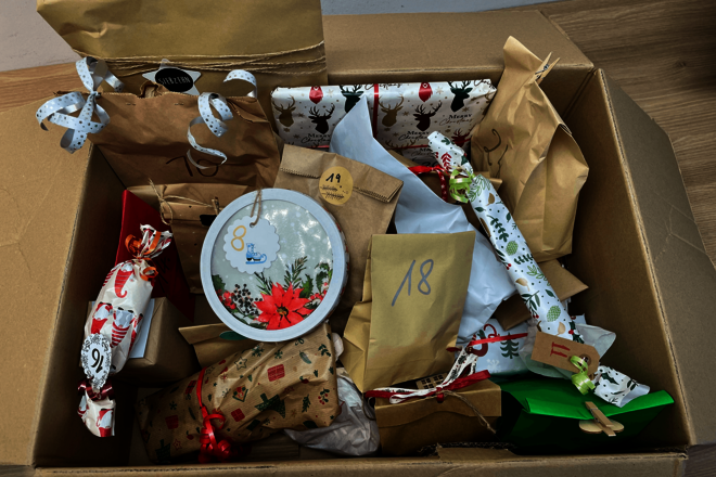 Blick von oben auf einen einen geöffneten Pappkarton. Darin sind verpackte Geschenke zu sehen. An einigen ist eine Zahl sichtbar.
