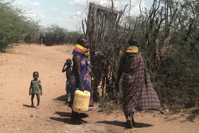 Zwei Frauen mit Wasserkanistern und zwei Kinder auf einer ausgetrockneten Straße