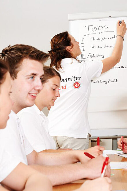 Eine Jugendliche erklärt am Whiteboard vor einer Gruppe anderer Jugendliche etwas