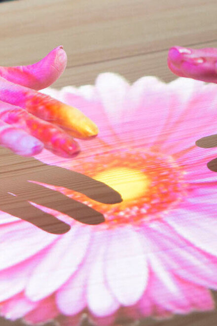 Hände auf einem  Blumenbild, das über die Tovertafel auf einen Tisch projiziert ist.