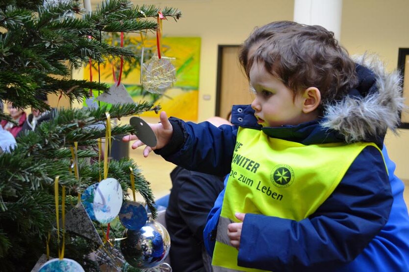 Ein kleiner Junge hängt Schmuck an den Weihnachtsbaum. 